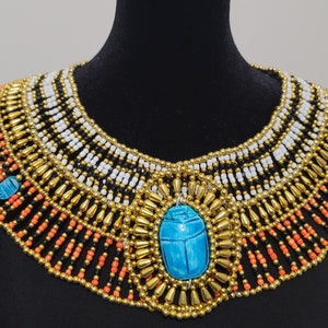 May include: A gold and black beaded necklace with a turquoise scarab beetle pendant. The necklace is layered with different sizes of beads and has a fringe of gold beads.