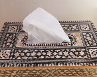 May include: A wooden tissue box cover with intricate inlaid mother-of-pearl designs in black and white. The box has a rectangular shape and a raised lid with a cutout for tissues.