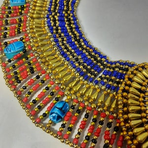 May include: A gold, red, black, and blue beaded necklace with scarab beetle charms. The necklace is made of small beads and has a layered design.