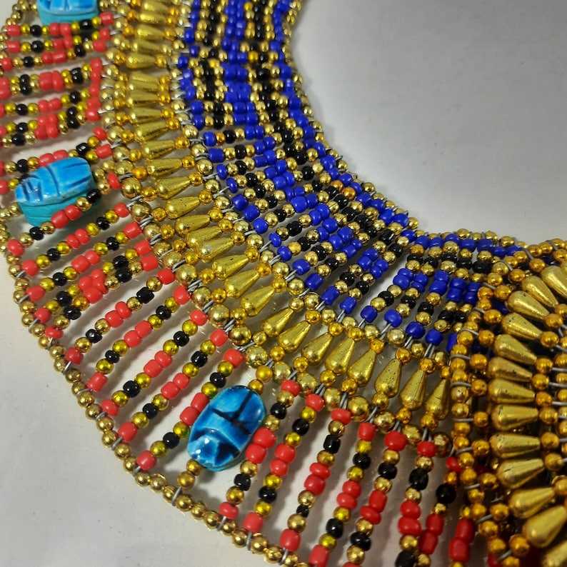 May include: A gold, red, black, and blue beaded necklace with scarab beetle charms. The necklace is made of small beads and has a layered design.