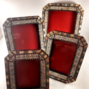 May include: Four decorative photo frames with a red backing. The frames have a geometric design with mother-of-pearl and dark accents. The frames are in various sizes and are arranged together.