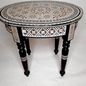 May include: A round, inlaid wood table with a black finish and intricate geometric patterns. The table has three legs and a small drawer.