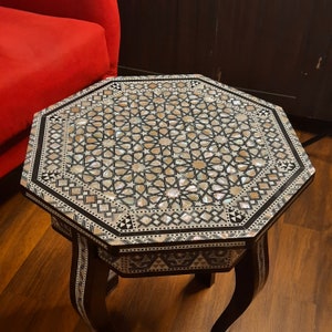 May include: Octagonal side table with intricate inlaid mother-of-pearl and wood design. The table has a dark brown finish and three legs.