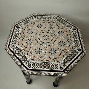 May include: Octagonal table with a geometric pattern inlaid with mother of pearl. The table has a dark wood base with three legs.