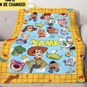 Puede incluir: Una manta de forro polar amarilla y azul con un patr&oacute;n de cuadr&iacute;cula y estrellas. La manta presenta personajes de la franquicia de pel&iacute;culas Toy Story, incluidos Woody, Buzz Lightyear, Jessie y el Sr. Potato Head. La manta est&aacute; personalizada con el texto "NAME" en una pancarta amarilla.