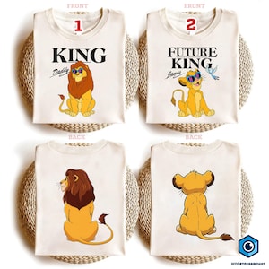May include: Off-white t-shirts with lion graphics. One shirt says "KING Daddy" with a lion wearing sunglasses. Another says "FUTURE KING" with a lion cub and bird. Backs of shirts show lion and cub.