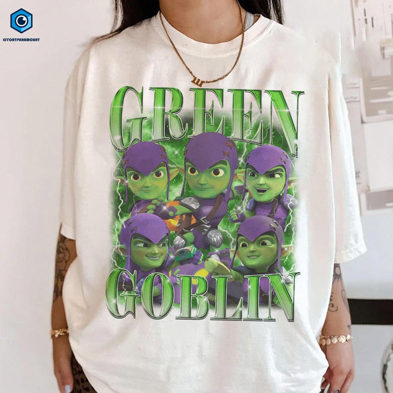 A white t-shirt with a graphic design featuring six green-skinned, purple-haired characters with googly eyes, along with the text "GREEN GOBLIN" prominently displayed.