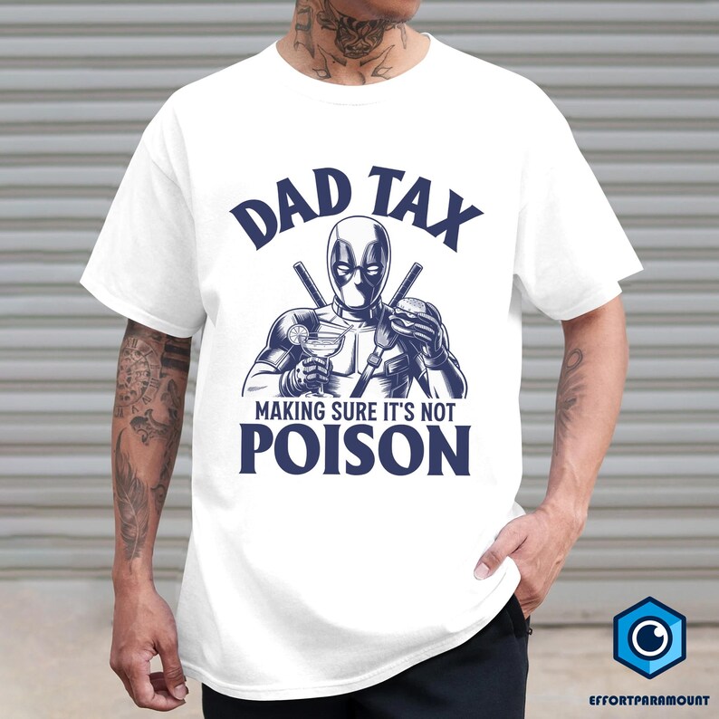 May include: White t-shirt featuring a graphic of a masked character holding a cocktail and a burger, with the text "DAD TAX MAKING SURE IT'S NOT POISON" in navy blue. The design is centered on the shirt.