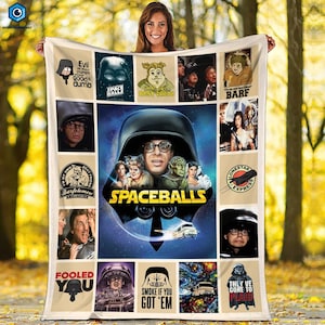 May include: A beige Spaceballs-themed blanket featuring various images and quotes from the movie. The central image is the movie poster, surrounded by character portraits and phrases like "Evil always triumphs because good is dumb."