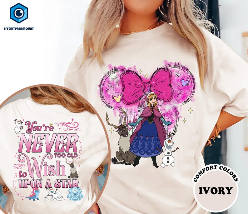 A white t-shirt with a graphic design featuring a girl in a blue dress and a pink bow, surrounded by various characters and elements.
