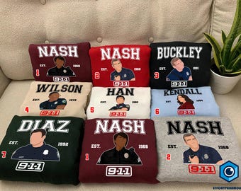 May include: Nine embroidered sweatshirts in various colours with the text "9-1-1" and the names of different characters. The sweatshirts are arranged in three rows of three.