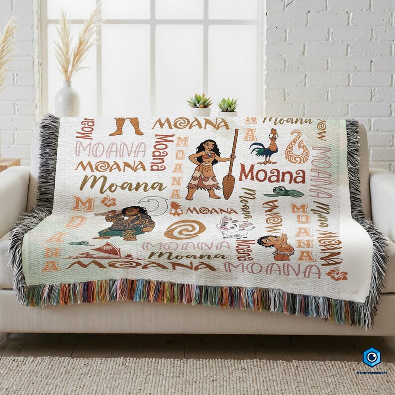 a cozy couch with a colorful throw blanket that has the word "Moana" printed on it. The blanket is adorned with various Moana characters and designs, creating a vibrant and playful atmosphere.