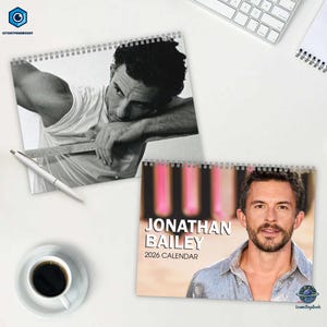 May include: Two spiral-bound calendars featuring images of a man. One is a black and white photo, the other has the text "JONATHAN BAILEY 2026 CALENDAR". A pen and a cup of coffee are also visible.