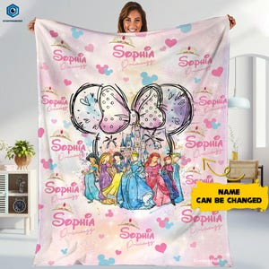 Puede incluir: Una manta rosa con un gran dise&ntilde;o de lazo, un castillo e ilustraciones de princesas. La manta tiene el nombre "Sophia Princess" repetido, junto con corazones y siluetas de Mickey Mouse. Tambi&eacute;n es visible el texto "NAME CAN BE CHANGED".