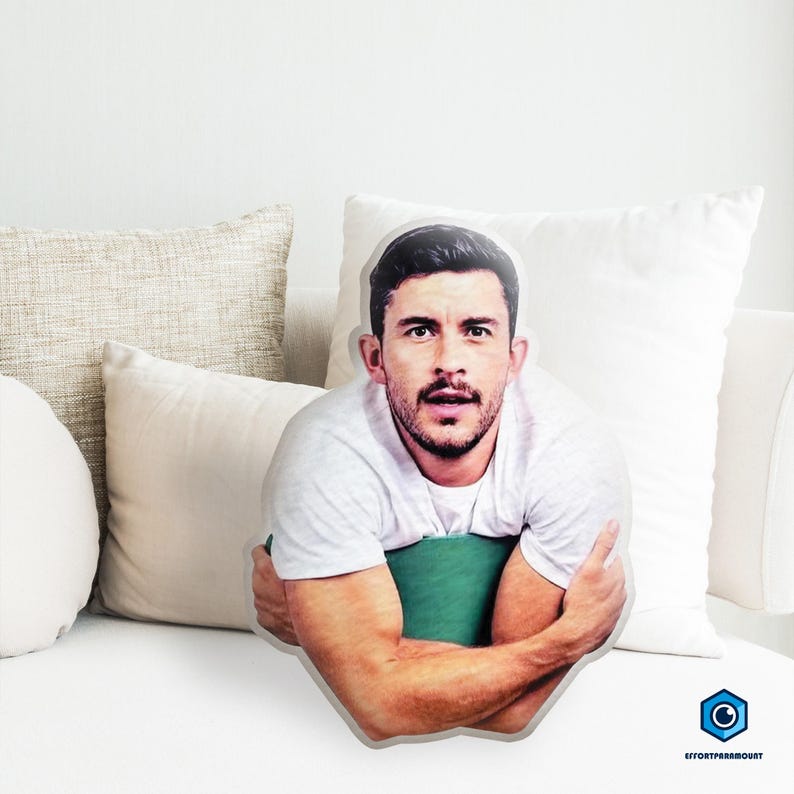 A man with a beard is sitting on a couch, surrounded by pillows.