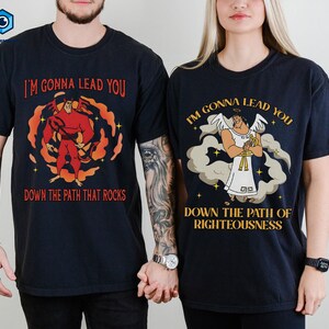 May include: Two navy blue t-shirts with matching graphics. One features a red devil figure with the text "I'm Gonna Lead You Down The Path That Rocks." The other shows an angel with the text "I'm Gonna Lead You Down The Path Of Righteousness."