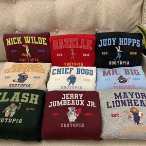 A collection of colorful hoodies or sweatshirts with various animal characters and text, including "NICK WILDE", "GAZELLE", "JUDY HOPPS", "CHIEF BOGO", "MA. BIG", "FLASH", "JERRY JUMBEAU JR.", and "MAYOR LIONHEART".
