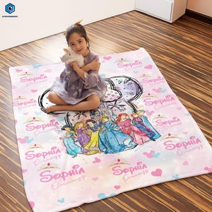 Puede incluir: Una manta rosa con tem&aacute;tica de princesas, con el nombre "Sophia Princess" repetido. Presenta ilustraciones de princesas y un castillo, con motivos de corazones y nubes.