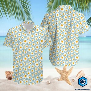 May include: A short-sleeved button-down shirt featuring a daisy pattern on a light blue background. The shirt has a classic collar and is displayed with a matching shirt, showcasing the all-over floral design. The design includes white daisies with yellow centers.