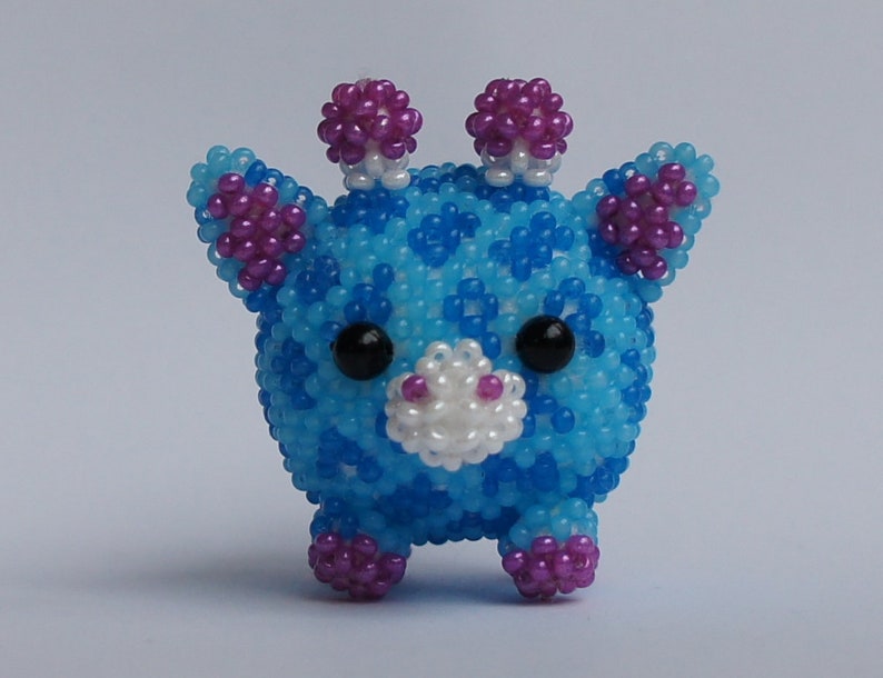 以下が含まれることがあります： 白のアクセントが付いた青と紫のビーズでできたキリンの玩具。キリンは丸い体と小さな脚をしています。