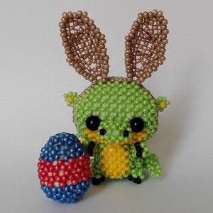 May include: A green and yellow beaded bunny with brown beaded ears holding a blue, red and white beaded Easter egg.