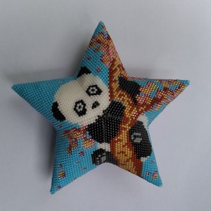 Könnte beinhalten: Ein blaues, sternförmiges Kissen mit einem Perlenmuster eines Pandabären, der an einem Baum mit rosa Blüten klettert.