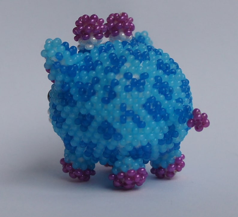 以下が含まれることがあります： 青と紫のビーズでできた小さな動物の置物。置物は丸い体と4本の足、そして頭の上に2つの小さな紫色のビーズの耳がついています。