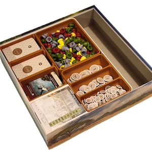 Könnte beinhalten: Eine braune Pappbox mit einem Spieleinsatz zum Organisieren von Spielteilen. Der Einsatz hat mehrere Fächer zum Verstauen von Karten, Spielsteinen und anderen Spielkomponenten. Die Box hat ein Landschaftsbild mit einer Bergkette und einem See auf dem Boden.