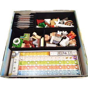 Peut inclure: Un organisateur de jeu de société avec des compartiments noirs contenant des pièces de jeu, des cartes et un plateau de jeu. Les pièces de jeu comprennent des bâtiments miniatures, des figurines et d'autres composants colorés. Le plateau de jeu comporte des pistes numérotées et des illustrations.