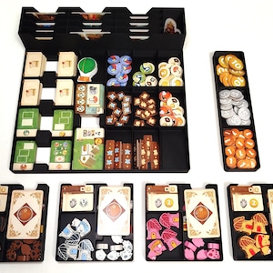 Op de afbeelding: Zwarte bordspellen organizer met meerdere compartimenten gevuld met spelstukken, kaarten en fiches. De stukken zijn in verschillende kleuren en vormen, waaronder houten fiches, kaarten en ronde fiches. De organizer is ontworpen om alle spelcomponenten te bevatten.