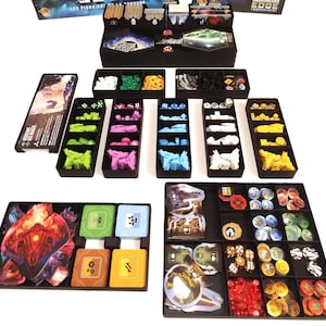 Peut inclure: Vue de dessus d'un organisateur de jeu de société avec divers plateaux noirs remplis de pièces de jeu. Les pièces sont de différentes couleurs, dont le vert, le rose, le bleu, le jaune et le blanc. Les pièces comprennent des dés, des jetons et des cartes.