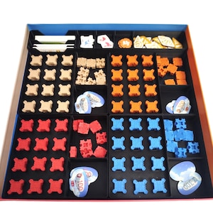 Op de afbeelding: Een bordspelorganizer met diverse spelstukken in een verdeelde doos. De stukken zijn in meerdere kleuren, waaronder rood, oranje, blauw en bruin. Er zijn ook spelgeldtokens met de nummers 100 en 300 erop gedrukt.