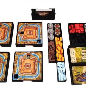 Peut inclure: Un organisateur de jeu de société avec divers composants. L'image montre quatre plateaux de jeu carrés avec un motif de château, ainsi que des jetons, des cartes et des pièces en bois dans des plateaux noirs. Les pièces du jeu sont de différentes couleurs.