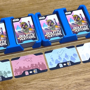 Könnte beinhalten: Vier blaue Kartenhalter mit Stapeln von Star Wars Bounty Hunters Karten. Die Karten zeigen ein Cartoon-Bild von Boba Fett. Es gibt vier weitere Karten mit verschiedenen Symbolen und Icons.