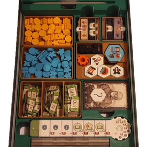 May include: A green organiser box with compartments for storing game pieces. The box contains various coloured wooden pieces, including yellow, blue, and green. There are also small cards with numbers and dollar signs, as well as a larger card with a portrait of a man.