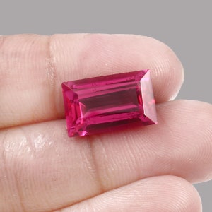 May include: A vibrant pink gemstone with a rectangular, emerald cut. The gemstone is faceted and has a high polish.
