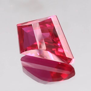 May include: A vibrant pink gemstone with a rectangular cut and a faceted design. The gemstone is set against a white background.