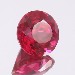 Puede incluir: Una gema roja vibrante con un corte redondo y un alto pulido. La gema está facetada y refleja la luz maravillosamente.