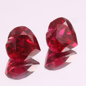 May include: Two heart-shaped ruby gemstones, each with a deep red color and a faceted cut.