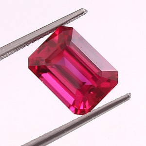 May include: A vibrant red emerald cut gemstone, held in tweezers, with a polished, faceted surface.
