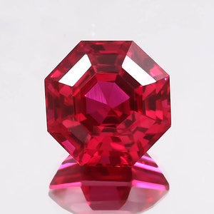 May include: A deep red octagon-shaped gemstone with a faceted cut. The gemstone is reflecting light and has a high shine.