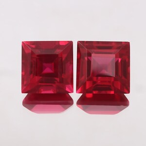 May include: Two square-shaped ruby gemstones, each with a red hue and a faceted cut.