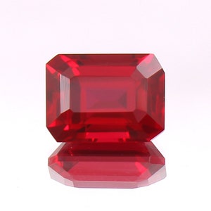 Puede incluir: Una piedra preciosa de color rojo intenso tallada en esmeralda con un acabado pulido.