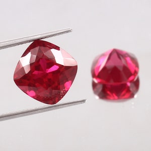 Könnte beinhalten: Zwei rote Edelsteine, einer quadratisch und einer rund, werden auf einer weißen Oberfläche gezeigt. Der quadratische Edelstein wird von einer Pinzette gehalten.