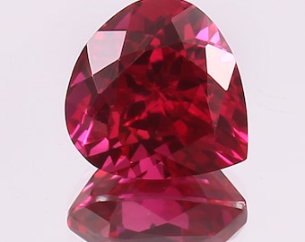 Puede incluir: Una gema de rubí facetada en forma de corazón. La gema es de un rojo intenso y saturado con múltiples facetas que reflejan la luz, creando un brillo brillante. El rubí se encuentra sobre una superficie reflectante.