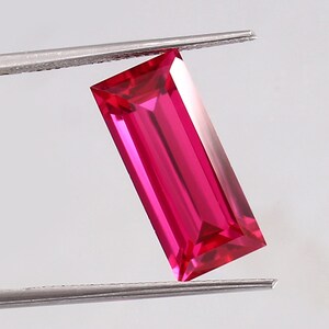 May include: A vibrant pink rectangular gemstone with a faceted cut, held by tweezers against a white background.