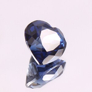 May include: A heart-shaped blue gemstone with a faceted cut. The gemstone is reflecting light, showing its brilliance.