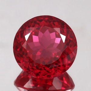 May include: A round, faceted, red gemstone with a star-shaped pattern inside.