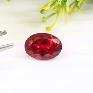 May include: A deep red oval gemstone with a faceted cut. The gemstone is set against a white background.