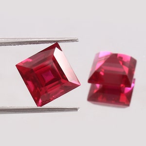 May include: Two red square-shaped gemstones with a faceted cut. The gemstones are held by tweezers.